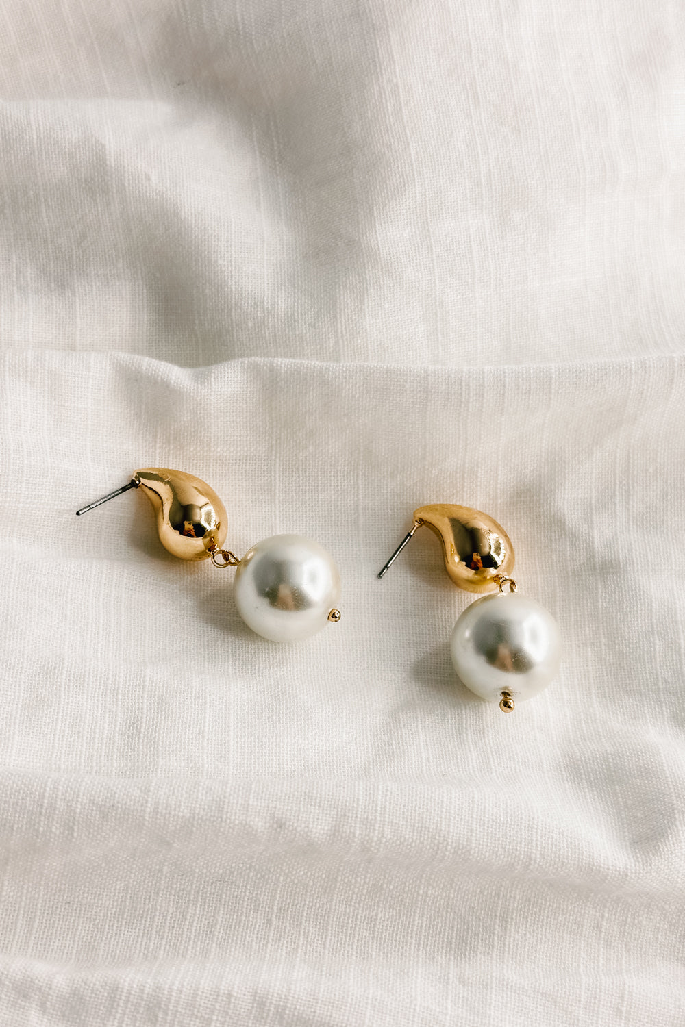 Flat lay view of the Julie Gold and Pearl Dangle Earring which features gold teardrop shape medallion linked with a pearl medallion