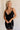 Front view of female model wearing the Sophia Black Plunge Neckline Mini Dress which features Black Lightweight Fabric, Mini Length, Side Ruched Detail with Covered Buttons Closure, Scoop Neckline, Adjustable Straps and Sleeveless