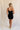 Full body back view of female model wearing the Sophia Black Plunge Neckline Mini Dress which features Black Lightweight Fabric, Mini Length, Side Ruched Detail with Covered Buttons Closure, Scoop Neckline, Adjustable Straps and Sleeveless