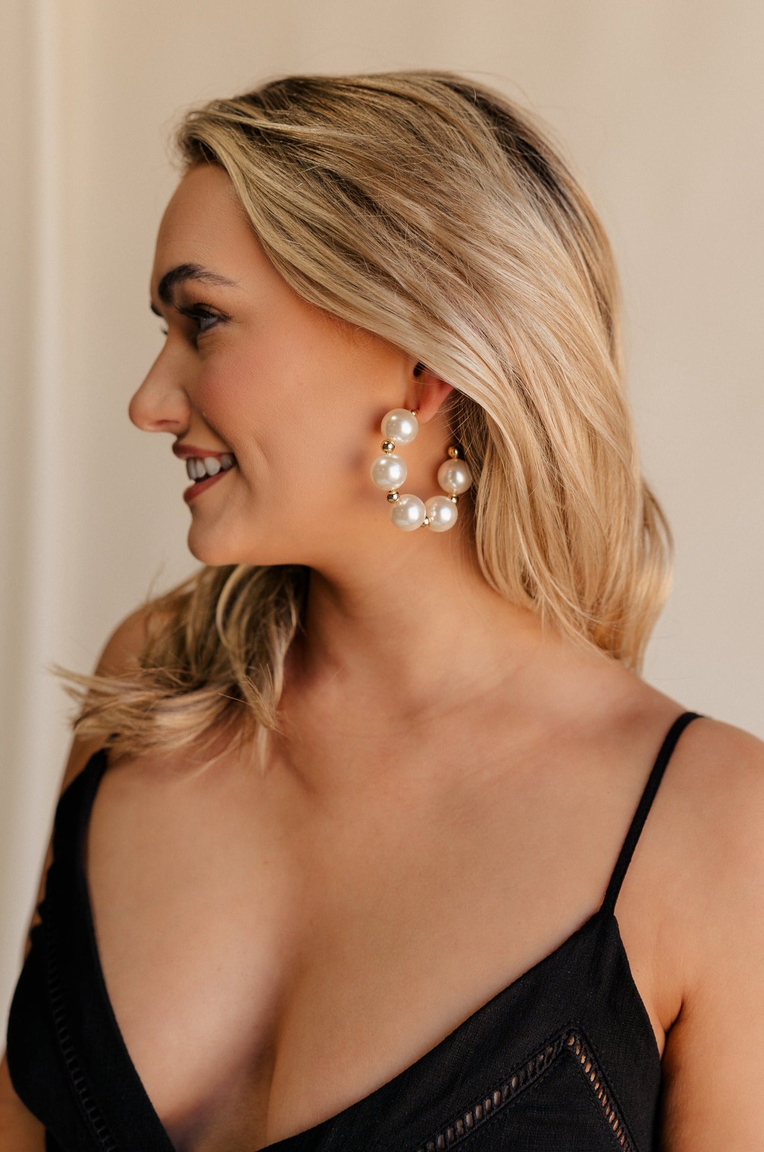 Side view of female model wearing the Delilah Pearl Hoop Earring which features oversized pearl beads with gold details and large open hoops with back closure