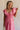 Front view of female model wearing the Gianna Ruffle Short Sleeve Tiered Maxi Dress in PInk which features Lightweight Fabric, Tiered Body, Midi Length, Pockets on each side, V-Neckline with a Tie Detail and Ruffle Short Sleeves. the dress is available in pink, aqua blue and white.