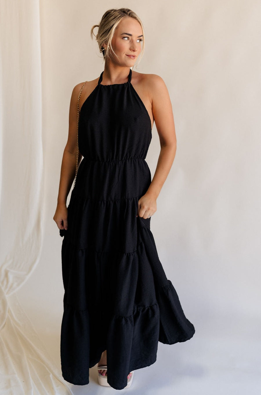 Full body view of female model wearing the Luna Halter Tie Tiered Maxi Dress in black which features  Lightweight Fabric, Tiered Body, Maxi Length, Thigh Length Lining, Halter Neckline with Tie  and Open Back