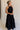 Full body side view of female model wearing the Luna Halter Tie Tiered Maxi Dress in black which features Lightweight Fabric, Tiered Body, Maxi Length, Thigh Length Lining, Halter Neckline with Tie and Open Back