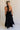 Full body back view of female model wearing the Luna Halter Tie Tiered Maxi Dress in black which features Lightweight Fabric, Tiered Body, Maxi Length, Thigh Length Lining, Halter Neckline with Tie and Open Back