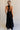 Full body back view of female model wearing the Luna Halter Tie Tiered Maxi Dress in black which features Lightweight Fabric, Tiered Body, Maxi Length, Thigh Length Lining, Halter Neckline with Tie and Open Back