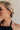 Side view of female model wearing the Ellie Gold Bow Dangle Earring which features gold bow shaped studs with back clasp closure