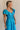 Side view of female model wearing the Gianna Ruffle Short Sleeve Tiered Maxi Dress in Blue which features Lightweight Fabric, Tiered Body, Midi Length, Pockets on each side, V-Neckline with a Tie Detail and Ruffle Short Sleeves. the dress is available in pink, aqua blue and white.