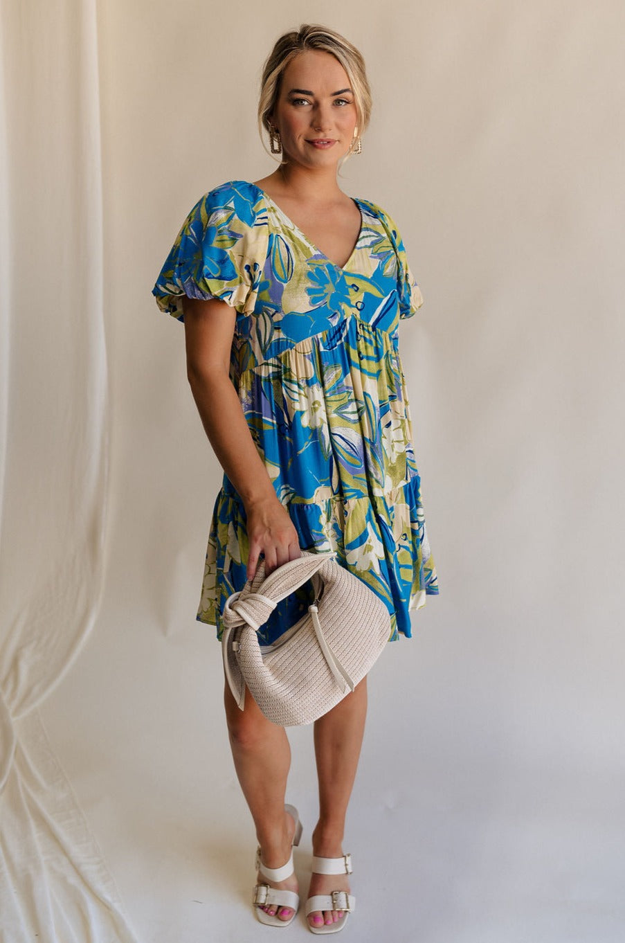 Full body view of female model wearing the Tessa Blue & Lime Green Floral Mini Dress which features Blue, Green and White Light Weight Fabric, Floral Print, Mini Length, Tiered Body, Blue Lining, V-Neckline and Short Puff Sleeves