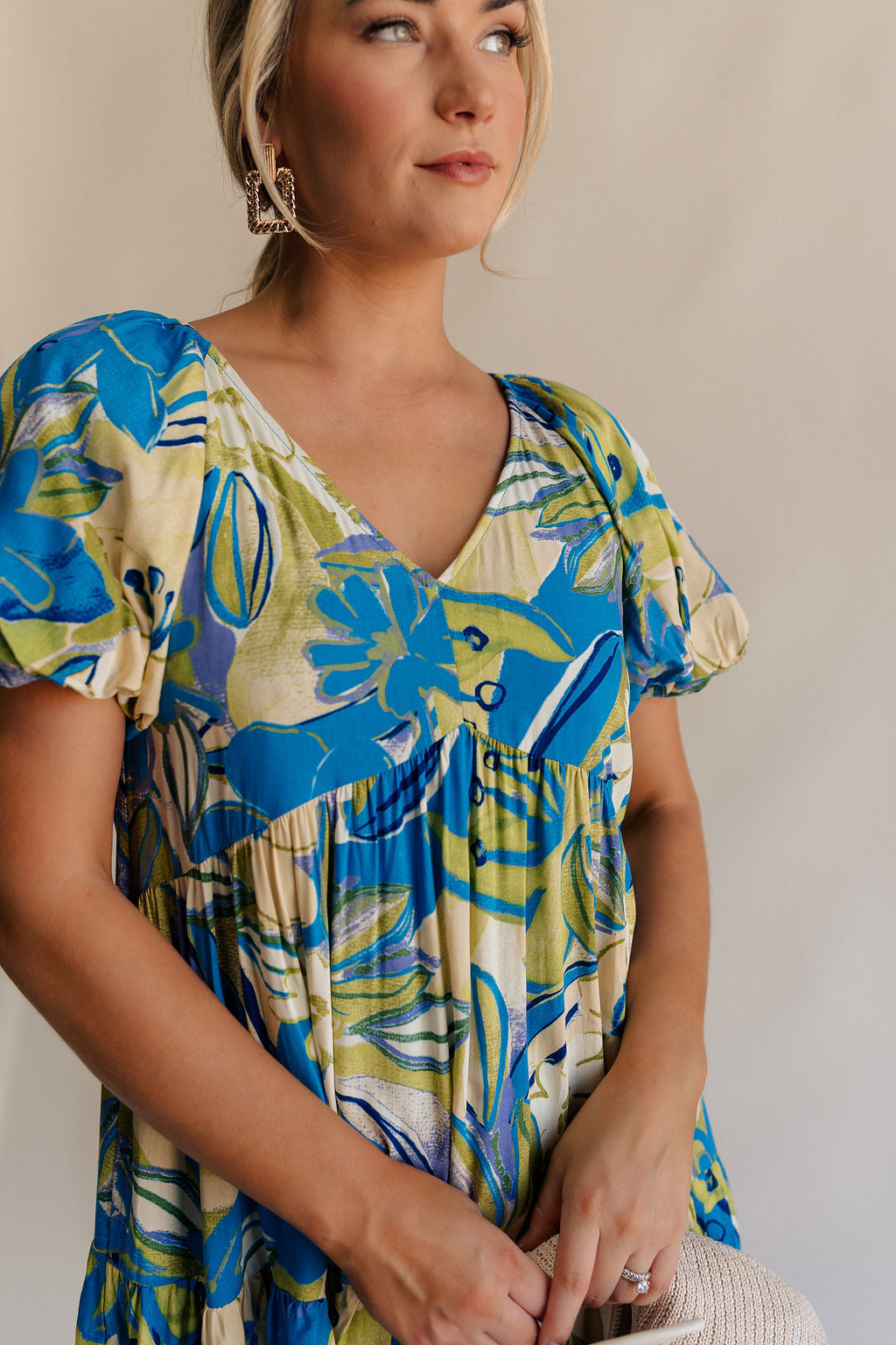 Close up front view of female model wearing the Tessa Blue & Lime Green Floral Mini Dress which features Blue, Green and White Light Weight Fabric, Floral Print, Mini Length, Tiered Body, Blue Lining, V-Neckline and Short Puff Sleeves