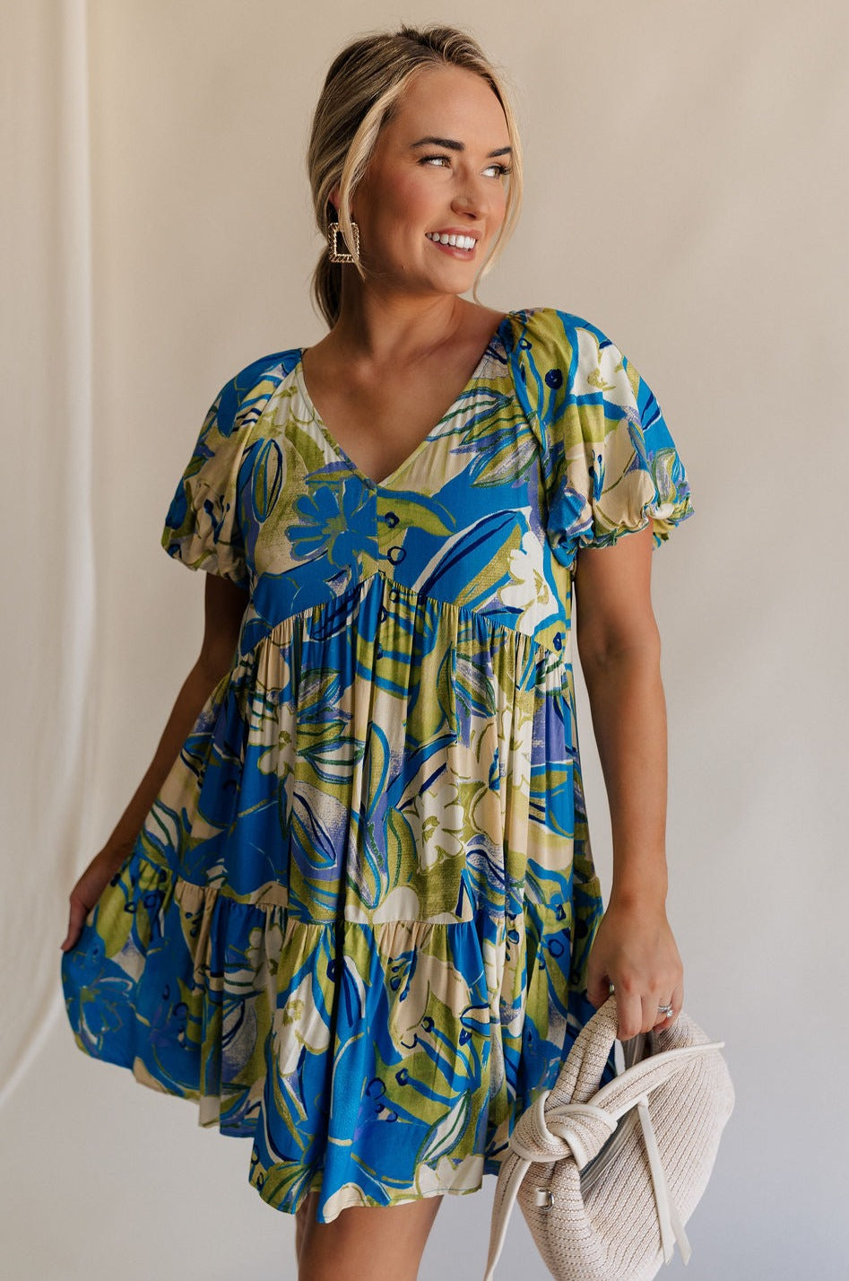 Front view of female model wearing the Tessa Blue & Lime Green Floral Mini Dress which features Blue, Green and White Light Weight Fabric, Floral Print, Mini Length, Tiered Body, Blue Lining, V-Neckline and Short Puff Sleeves