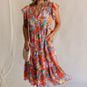 Full body view of female model wearing the Kai Orange Multi Floral Midi Ruffle Dress which features Orange, Blue, Green, Purple and Yellow Lightweight Fabric, Floral Design, Tiered Body, Orange Lining, Midi Length, Pockets On Each Side, V-Neckline and Ruffle Short Sleeves
