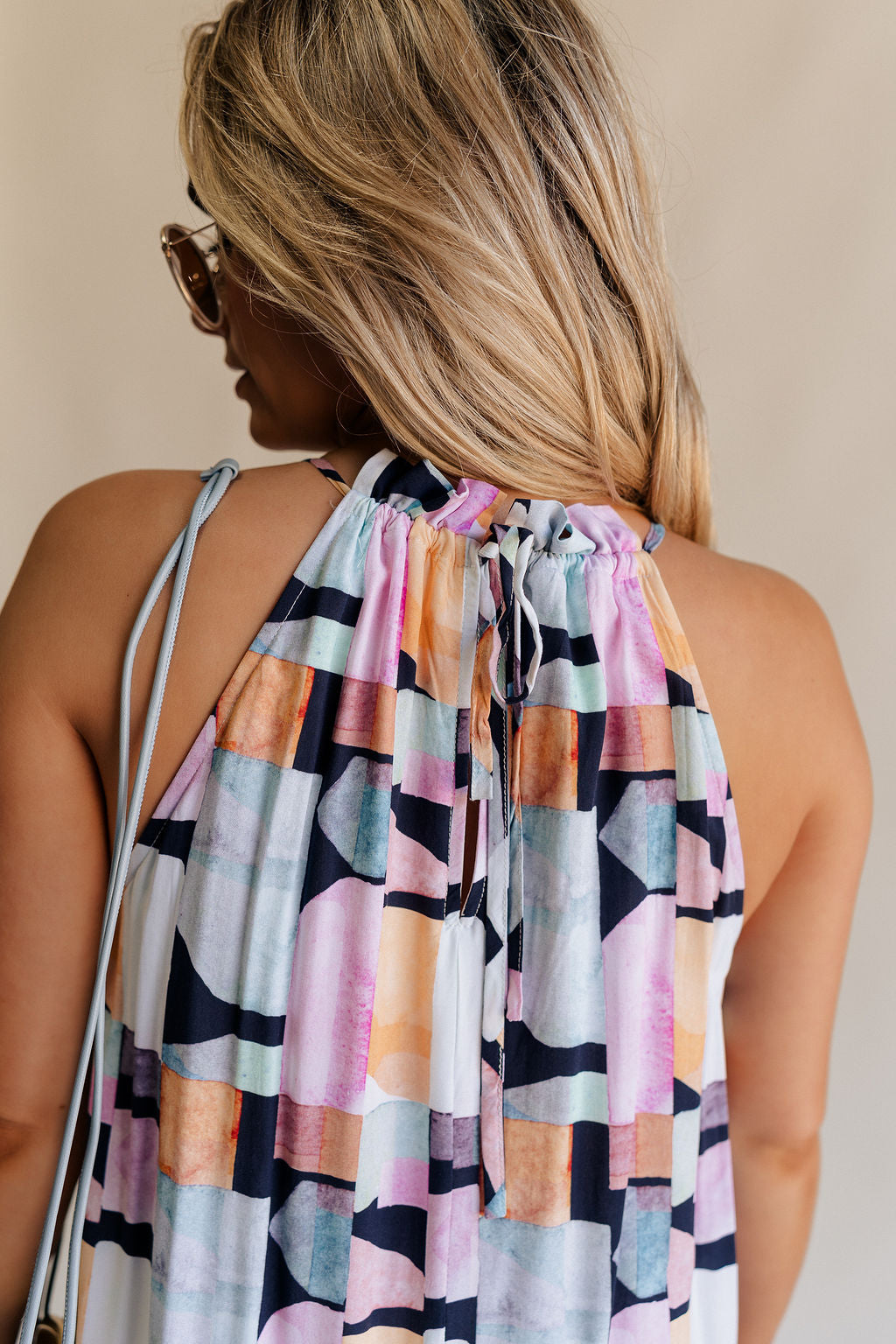 Back view of female model wearing the Emily Black Multi Geometric Halter Maxi Dress which features Black, Blue, Orange, Pink and White Lightweight Fabric, Geometric Pattern, Maxi Length, White Thigh Length Lining, Ruffle Hem and Halter Neckline with Back Tie Strap