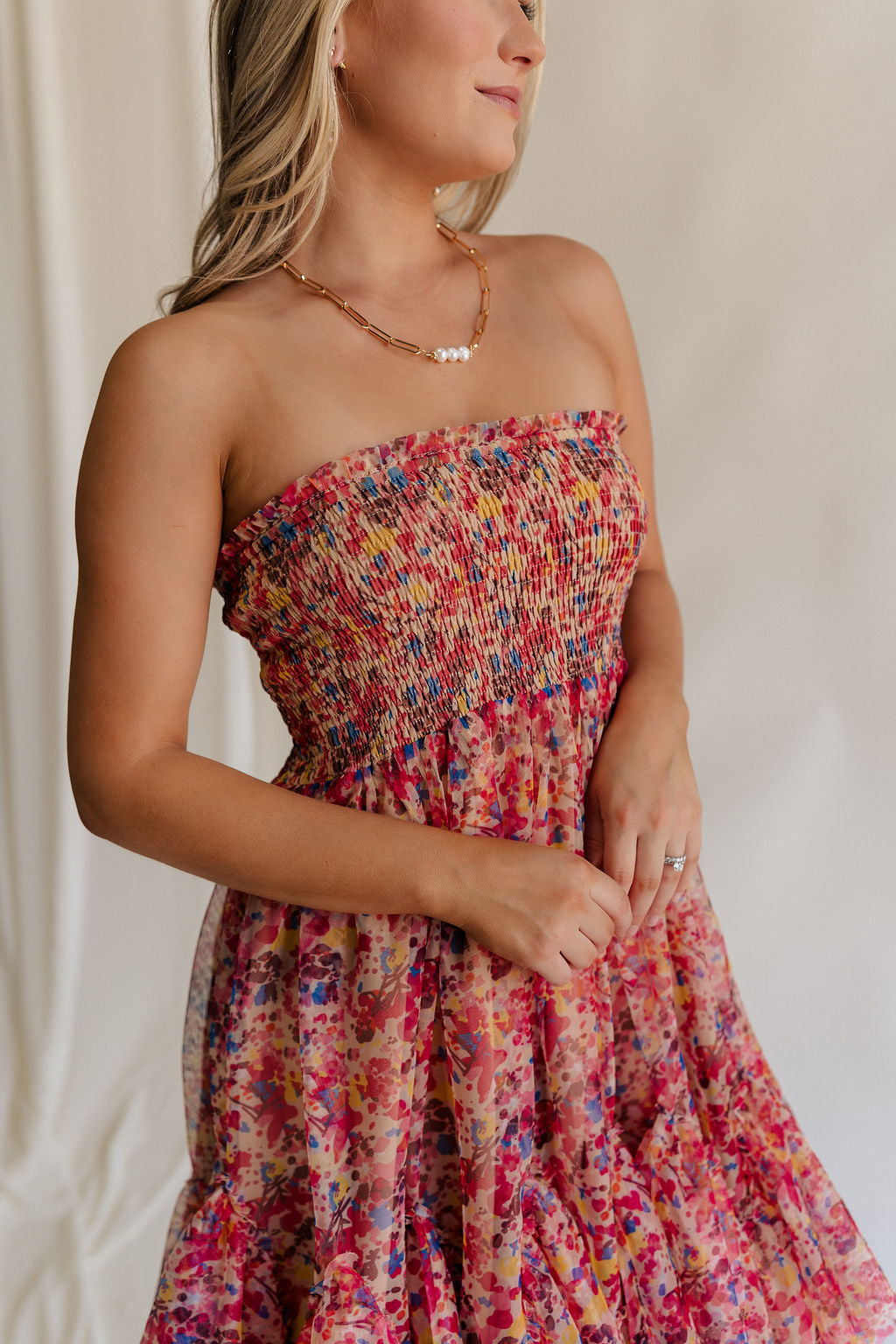 Close up side view of female model wearing the Charlie Pink Multi Floral Flare Mini Dress which features Brown, Pink, Yellow, Blue and Tan Sheer Fabric, Floral Print, Ruffle Hem, Tan Lining, Midi Length and Smocked Upper