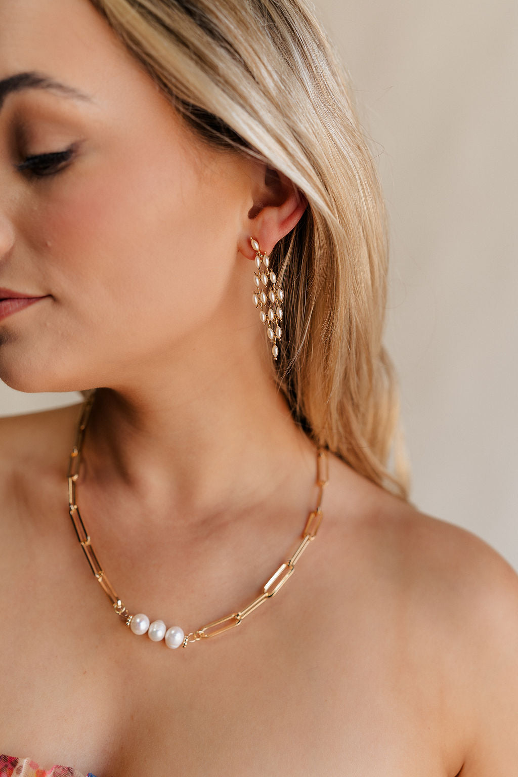 Close up side view of female model wearing the Gracie Pearl & Gold Dangle Earring which features pearls set in gold, dangle pearls linked together and back closure