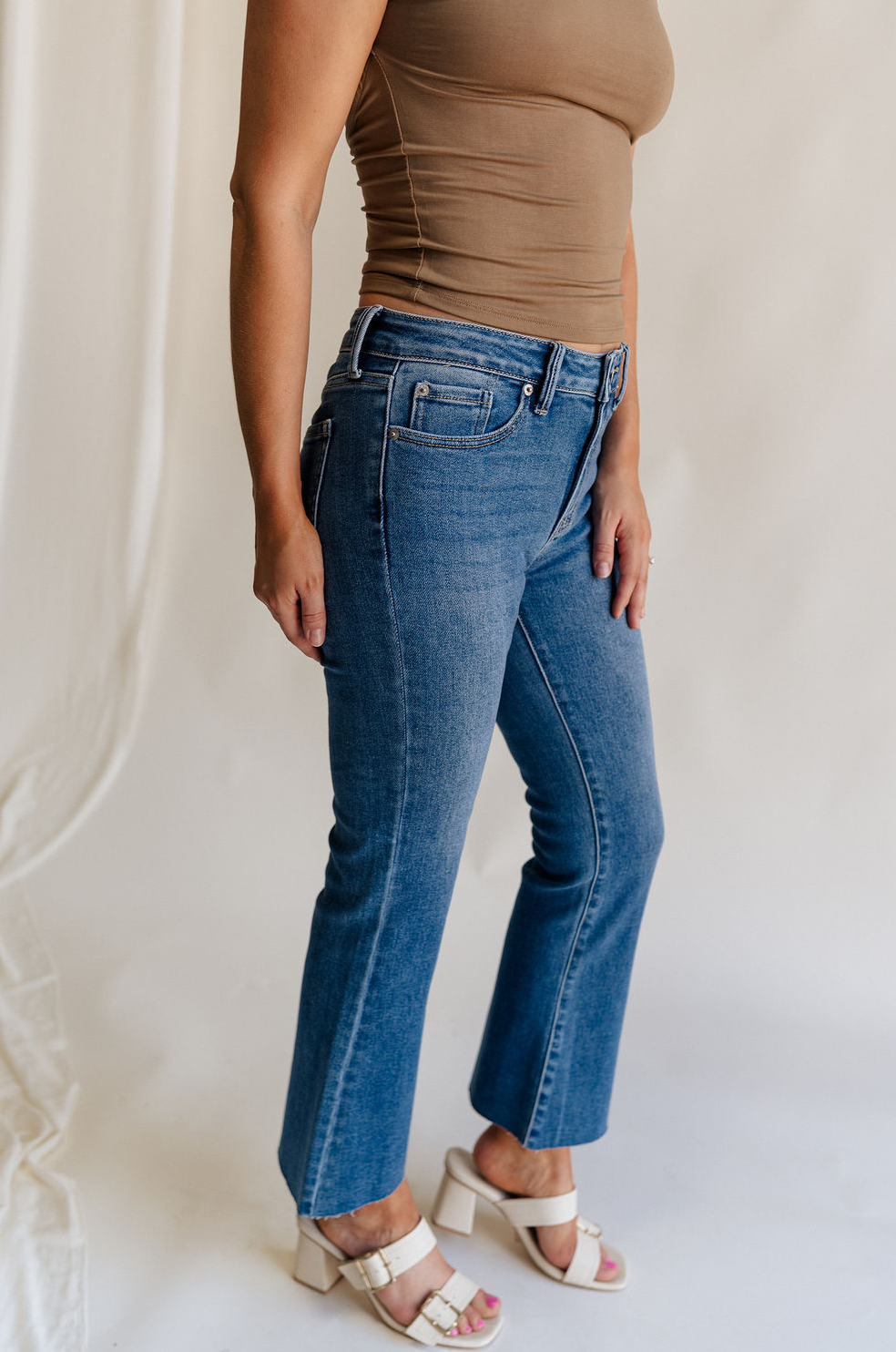 Side view of female model wearing the Emerson Medium Wash Straight Leg Jeans which features Medium Wash Denim, Two Front Pockets, Two Back Pockets, Front Zipper with Button Closure, Belt Loops and Straight Pant Legs