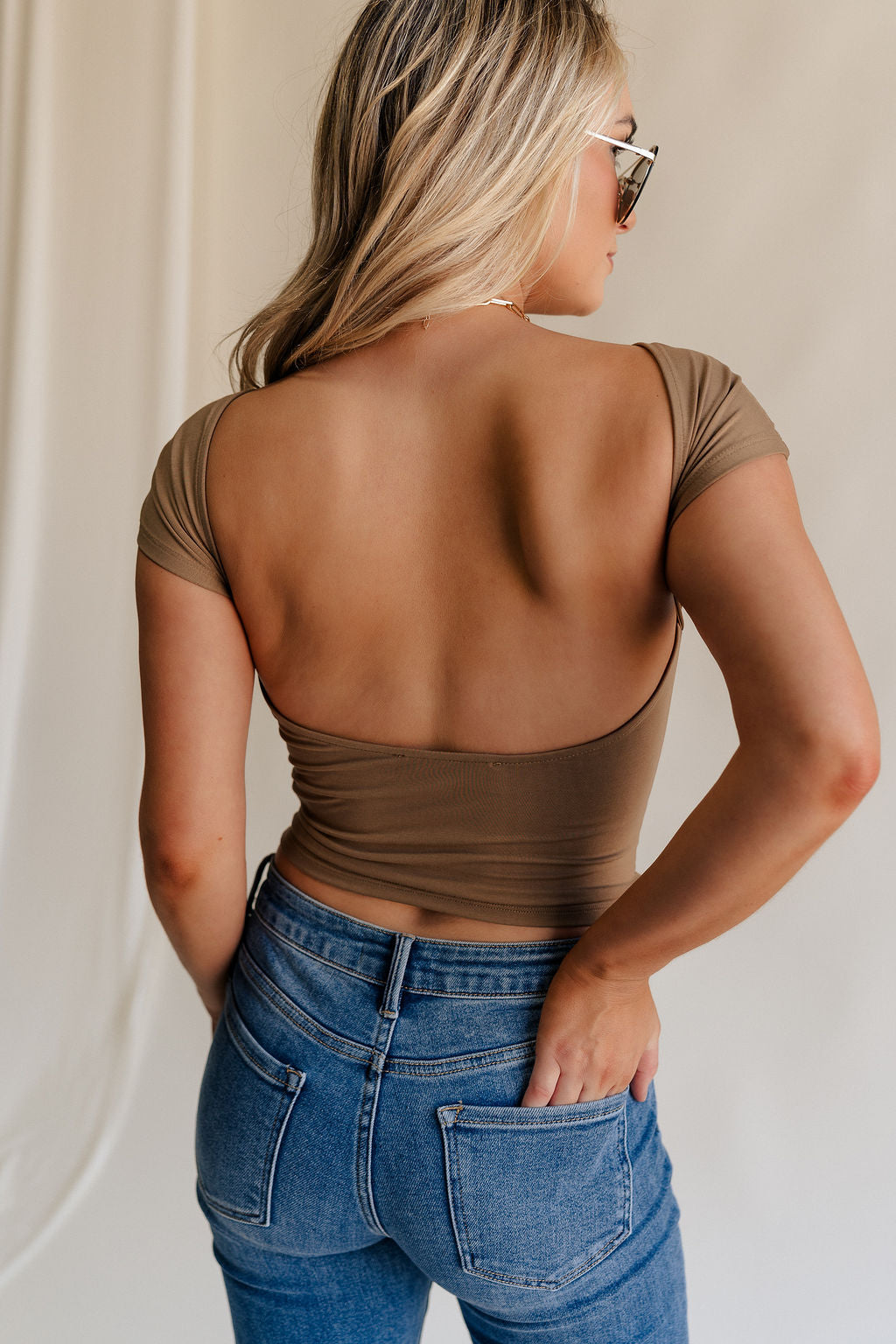 Back view of female model wearing the Sloane Mocha Brown Open Back Top which features Mocha Brown Lightweight Fabric, Short Sleeves, Round Neckline and Scoop Back