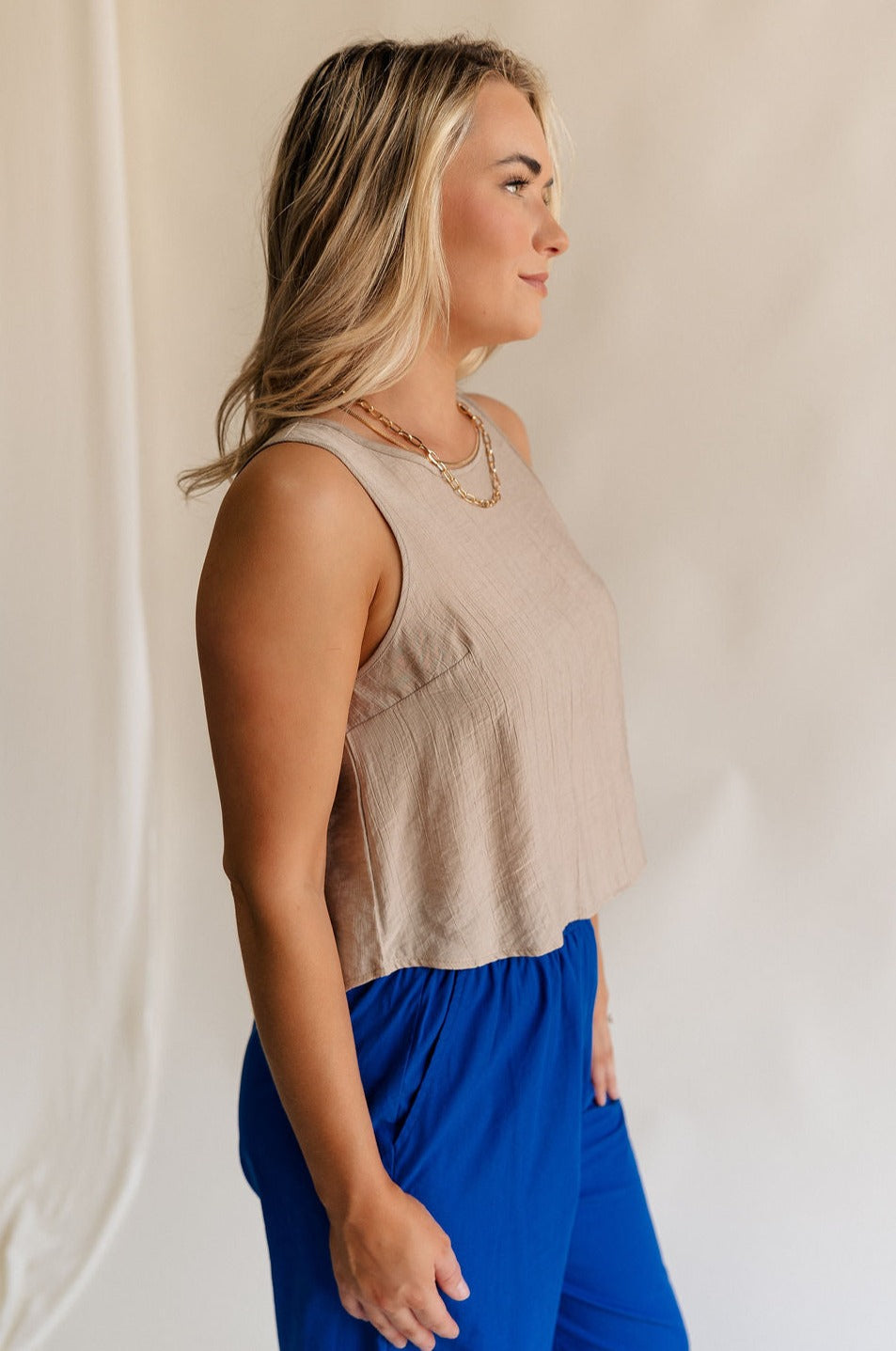 Side view of female model wearing the Sienna Light Taupe Sleeveless Tank which features Lightweight Taupe Fabric, Round Neckline, Sleeveless and Back Key Hole with Button Closure