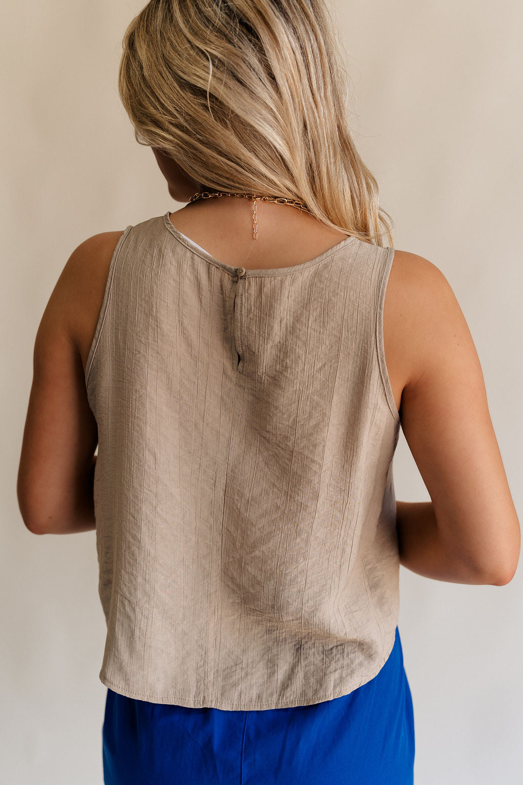 Back view of female model wearing the Sienna Light Taupe Sleeveless Tank which features Lightweight Taupe Fabric, Round Neckline, Sleeveless and Back Key Hole with Button Closure
