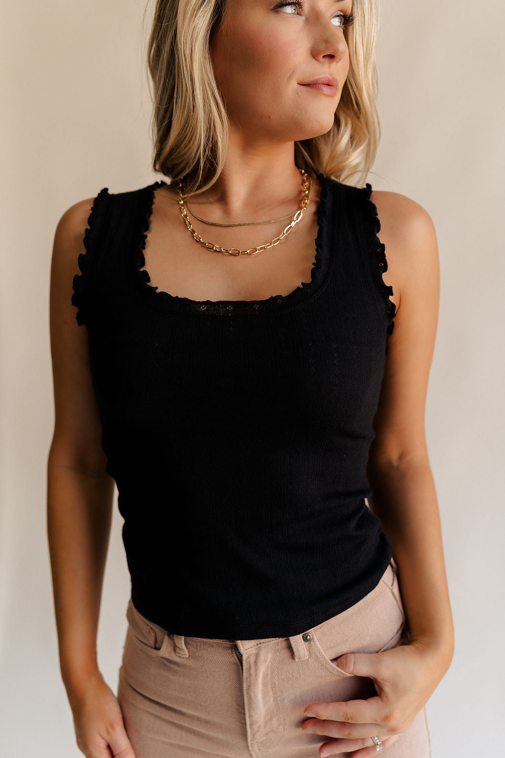 Close up front view of female model wearing the Myla Black Ruffle Sleeveless Tank which features Black Knit Fabric, Lettuce Hem Details, Round Neckline and Sleeveless