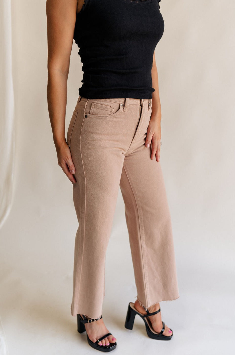 Side view of female model wearing the Lena Light Taupe Wide Cropped Leg Pants which features Light Taupe Denim Fabric, Wide Pant Leg, Raw Hem, Front Zipper with Button Closure, Two Front Pockets, Two Back Pockets and Belt Loops