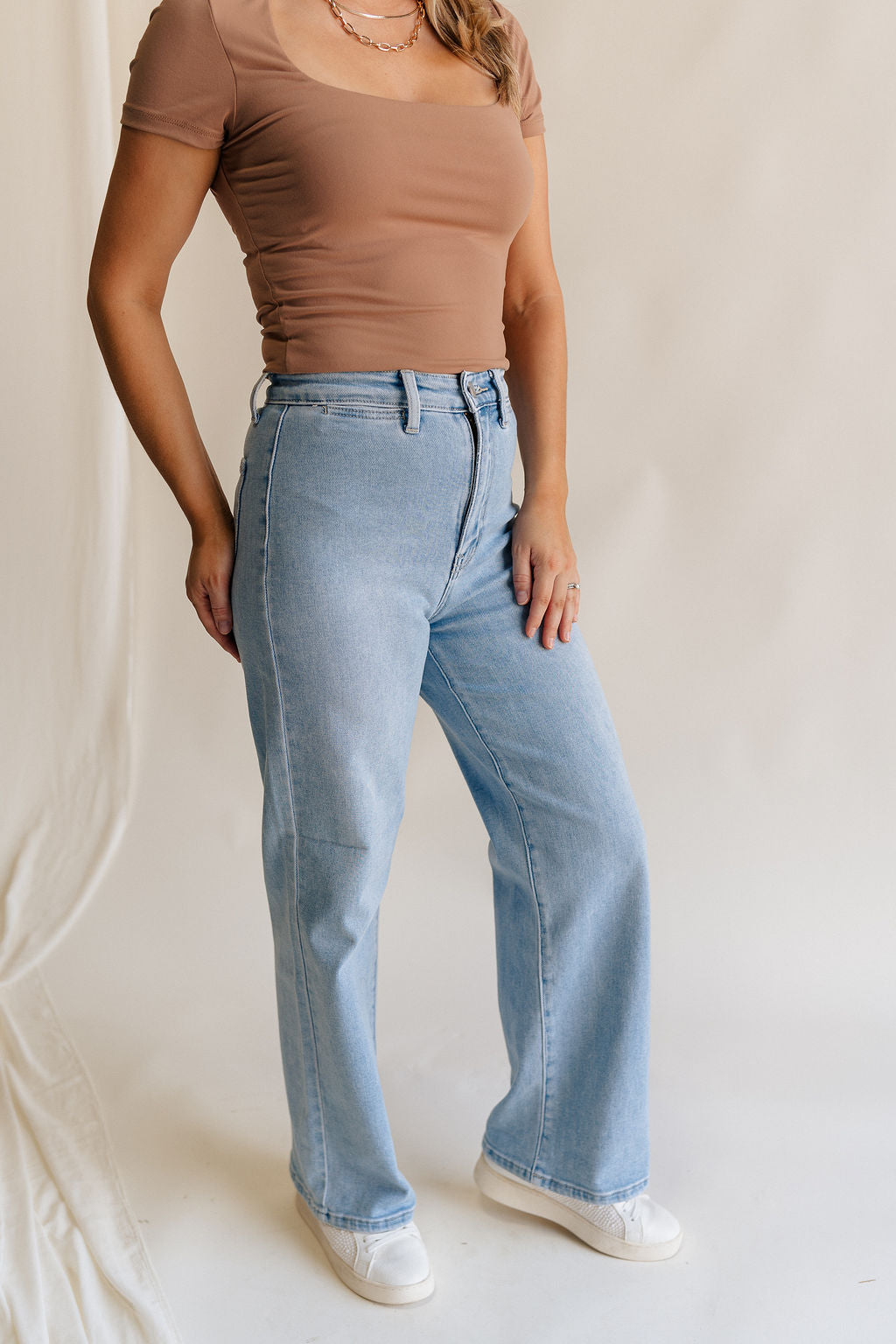 Frontal side view of female model wearing the Stevie Light Denim Wash Wide Leg Jeans which features Light Denim Wash Fabric, Two Front Pockets, Two Back Pockets, Front Zipper with Button Closure, Belt Loops and Wide Pant Legs