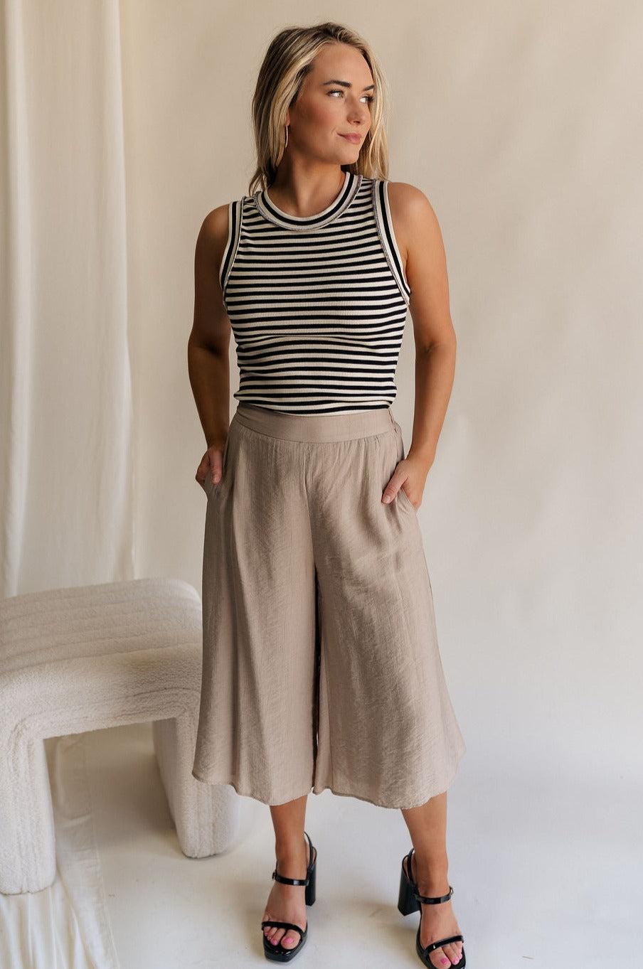 Full body view of female model wearing the Sienna Light Taupe Cropped Flare Pants which features Lightweight Taupe Fabric, Taupe Lining, Cropped Wide Pant Legs, Pockets on each side and Back Elastic Waistband