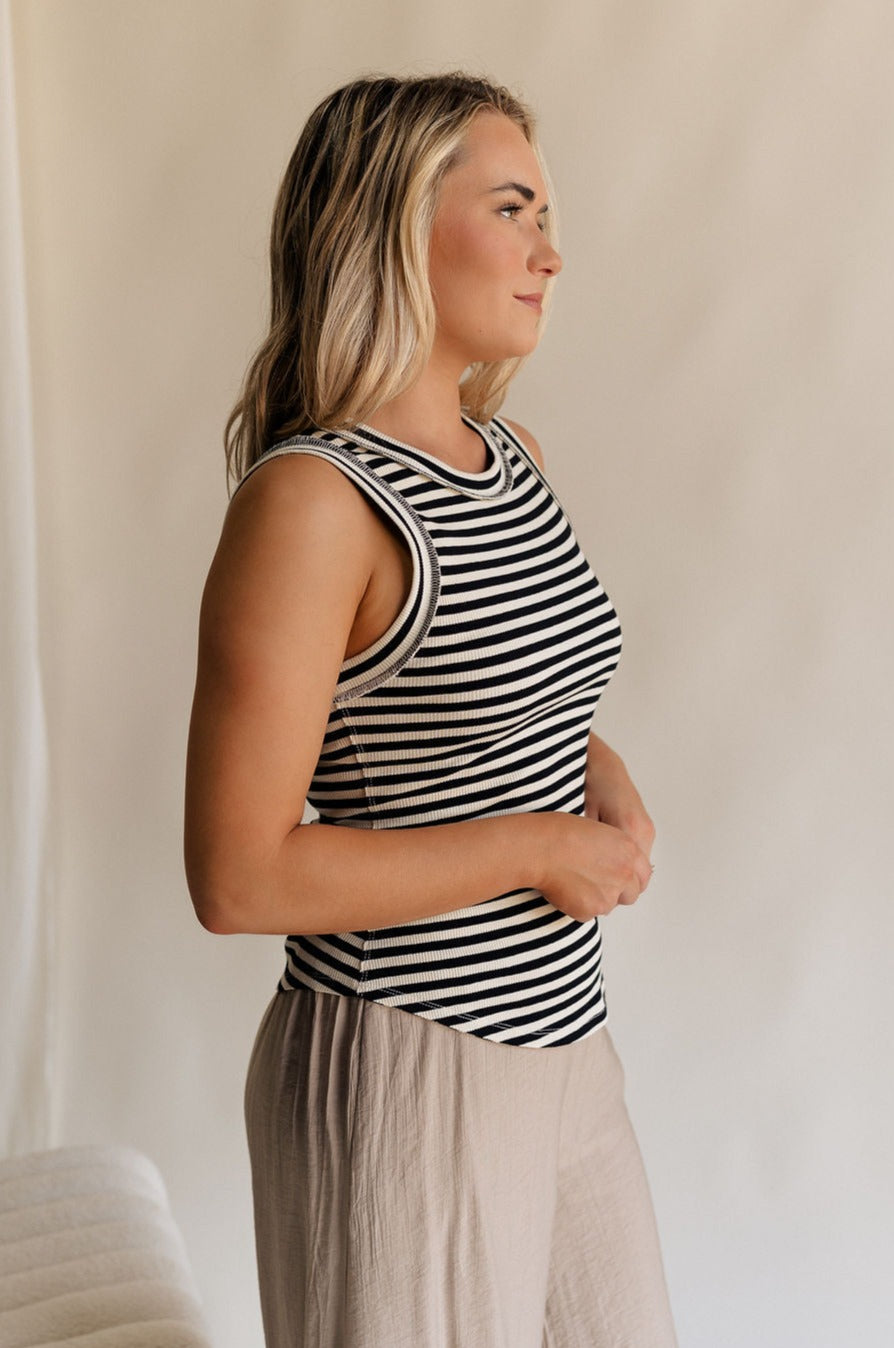 Side view of female model wearing the Lilah Black & Cream Stripe Sleeveless Tank which features Black and Cream Knit Fabric, Stripe Pattern, Round Neckline and Sleeveless
