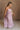 Full body side view of female model wearing the Imani Lavender Maxi Dress that has lavender fabric, thin straps, and a ruffled maxi hem.