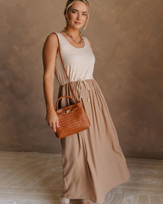 Full body front view of female model wearing the Bristol Mocha & Tan Maxi Dress that has a tan knit upper with thick straps, a mocha maxi skirt, and a drawstring waist. Worn with brown purse.