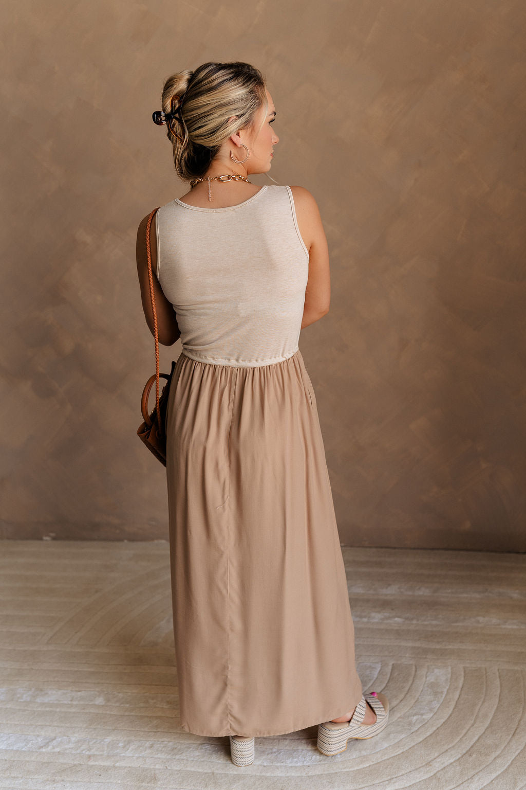 Full body back view of female model wearing the Bristol Mocha & Tan Maxi Dress that has a tan knit upper with thick straps, a mocha maxi skirt, and a drawstring waist. 