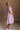 Full body side view of female model wearing the Cameron Pink & White Striped Dress that has pink and white vertical striped fabric, short puff sleeves, a tiered skirt, and button up front.