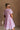 Upper body back/side view of female model wearing the Cameron Pink & White Striped Dress that has pink and white vertical striped fabric, short puff sleeves, a tiered skirt, and button up front.