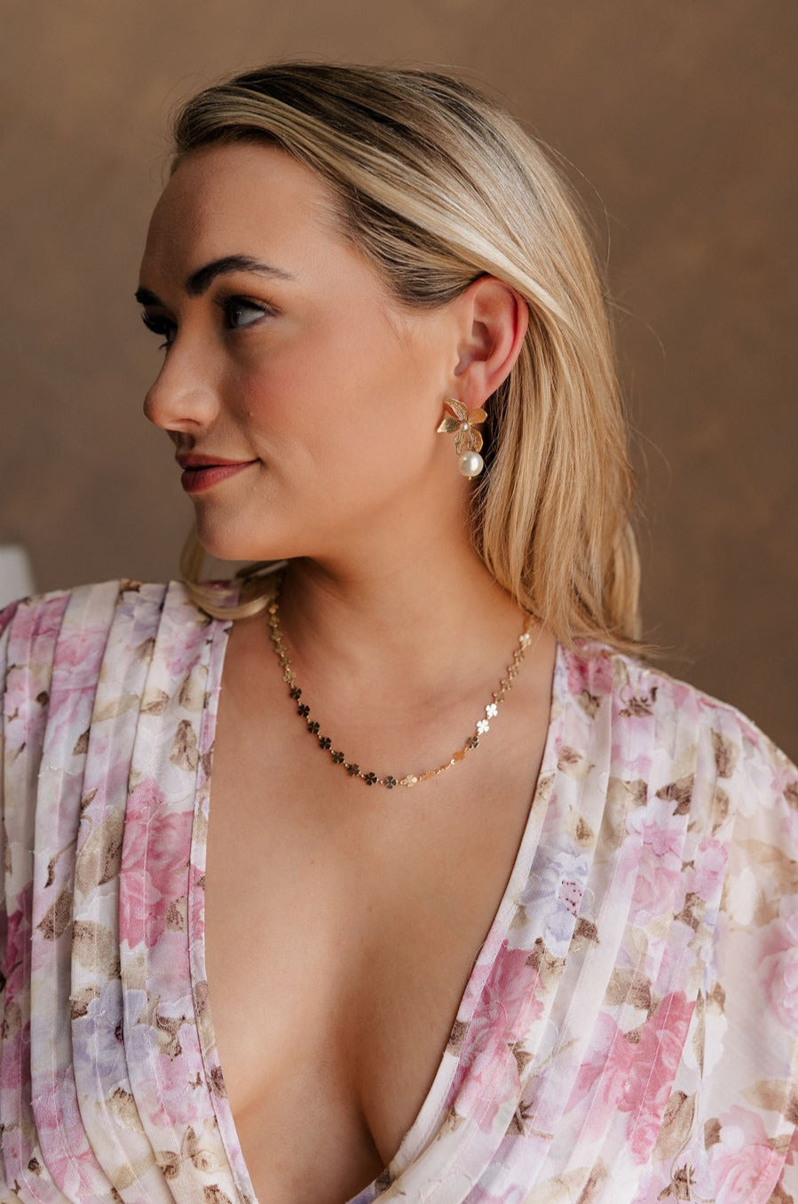 Side view of female model wearing the Mina Gold Floral & Pearl Dangle Earring which features gold flower shaped stud linked with a pearl dangle medallion