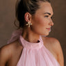 Side view of female model wearing the Lucia Gold Ribbed Bow Studs which features  gold ribbed bows with back clasp closure