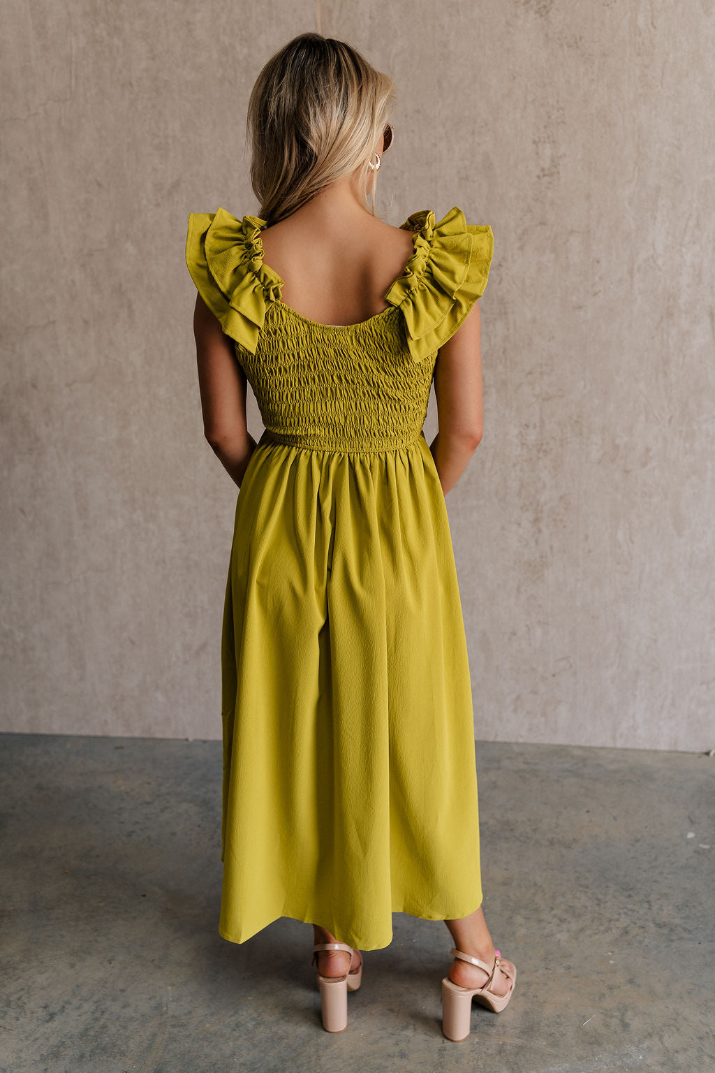 Upper body back view of female model wearing the Kristina Chartreuse Smocked Sleeveless Midi Dress that has chartreuse fabric with a smocked upper, ruffle straps, and a midi length hem.