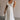 Full body front view of female model wearing the Gianna Ruffle Short Sleeve Tiered Maxi Dress in White which features Lightweight Fabric, Tiered Body, Midi Length, Pockets on each side, V-Neckline with a Tie Detail and Ruffle Short Sleeves. the dress is available in pink, aqua blue and white.