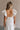 Back view of female model wearing the Gianna Ruffle Short Sleeve Tiered Maxi Dress in White which features Lightweight Fabric, Tiered Body, Midi Length, Pockets on each side, V-Neckline with a Tie Detail and Ruffle Short Sleeves. the dress is available in pink, aqua blue and white.