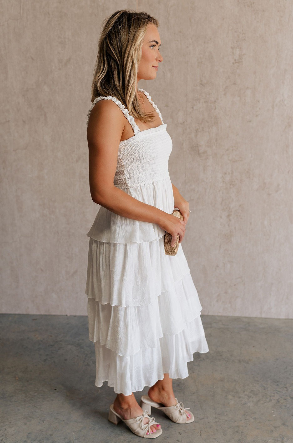 Full body side view of female model wearing the Nova Smocked Tiered Midi Dress which features Lightweight Fabric, Fully Lined, Tiered Ruffle Body, Smocked Upper, Square Neckline and Elastic Straps.