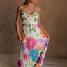 Full body front view of model wearing the Alia Pleated Floral Maxi Dress that has multi-colored fabric with a floral print, pleating, thin straps, and a sweetheart neck. Model is holding skirt.