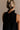 Close-up upper body back view of female model wearing the Mara Sleeveless Mock Neck Tie Back Dress in Black that has a ruffle mock neck, mini length hem, and tie back.