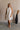 Full body front view of female model wearing the Mara Sleeveless Mock Neck Tie Back Dress in Off White that has a ruffle mock neck, mini length hem, and tie back.