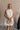 Upper body front view of female model wearing the Mara Sleeveless Mock Neck Tie Back Dress in Off  White that has a ruffle mock neck, mini length hem, and tie back.