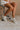 Side view of female model wearing the Alta Sneaker in Off White which features light grey and white suede upper fabric, white sole, and lace up details