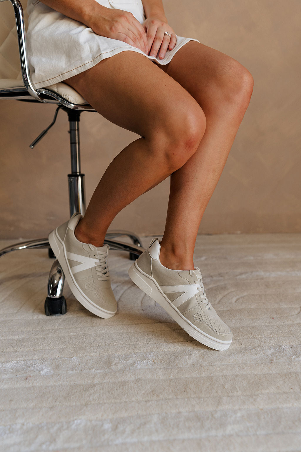 Side view of female model wearing the Alta Sneaker in Off White which features light grey and white suede upper fabric, white sole, and lace up details