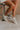 Side view of female model wearing the Alta Sneaker in Off White which features light grey and white suede upper fabric, white sole, and lace up details