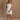 Full body front view of female model wearing the Kelsey White Denim Romper that has white denim fabric, a strapless neck, and a pleated skirt over shorts lining.