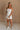 Full body front view of female model wearing the Kelsey White Denim Romper that has white denim fabric, a strapless neck, and a pleated skirt over shorts lining.