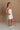 Full body side view of female model wearing the Kelsey White Denim Romper that has white denim fabric, a strapless neck, and a pleated skirt over shorts lining.
