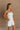 Upper body side view of female model wearing the Kelsey White Denim Romper that has white denim fabric, a strapless neck, and a pleated skirt over shorts lining.