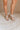 Front side view of female model wearing the Sofft Camille Sandal in Tapioca Grey which features light grey upper fabric, Side zipper with matching leather pull, cross straps and stacked block heel